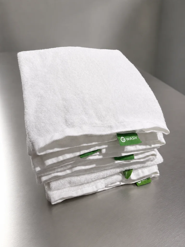 Folded white bath towels with green eWASH labels
