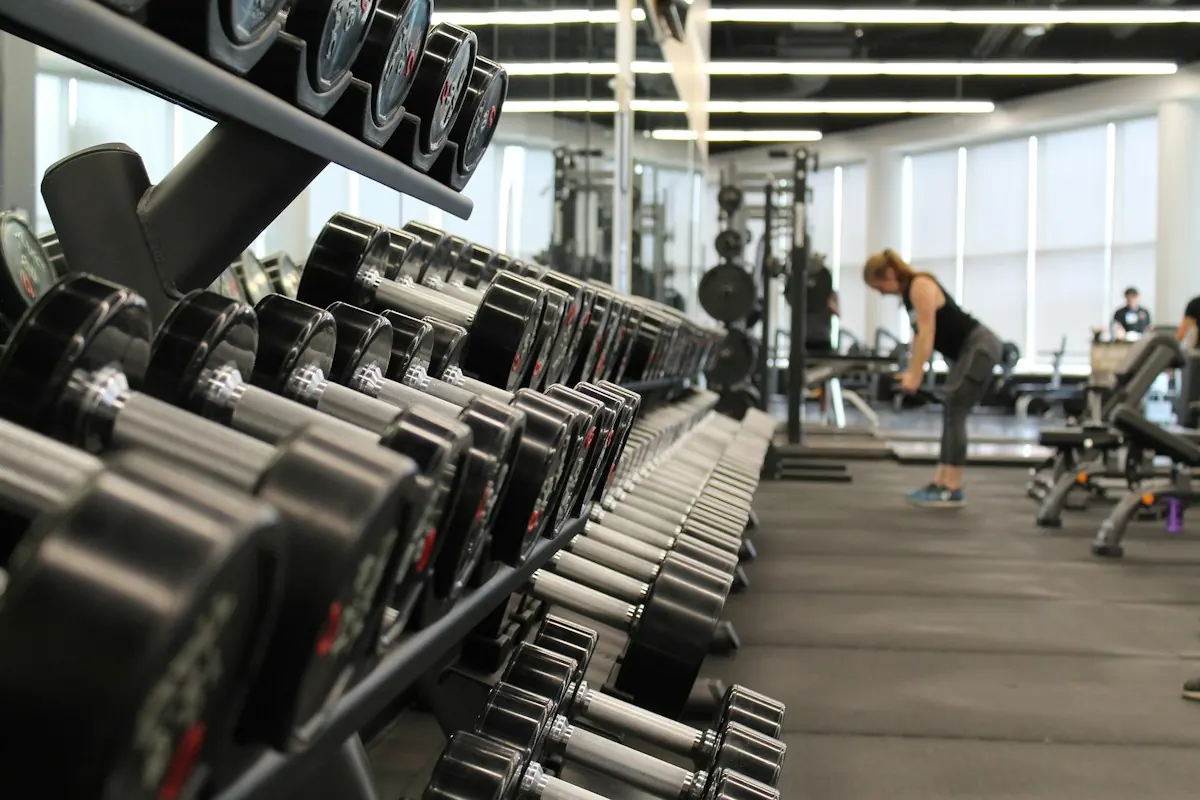Racks of dumbbells in a gym with a person training in the background