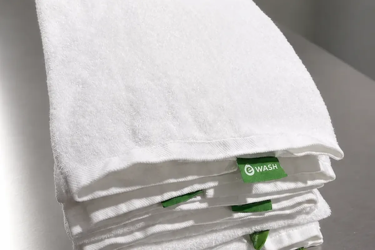 Folded white bath towels with green eWASH labels