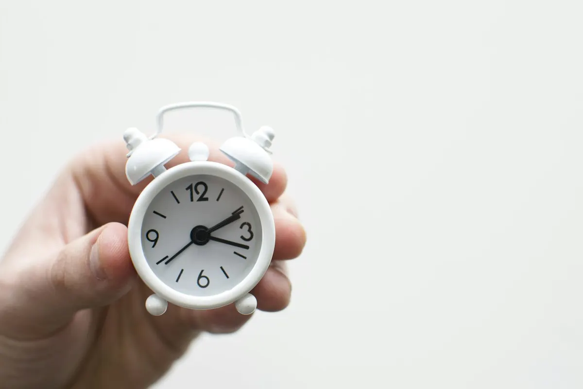 Hand holding a small white alarm clock
