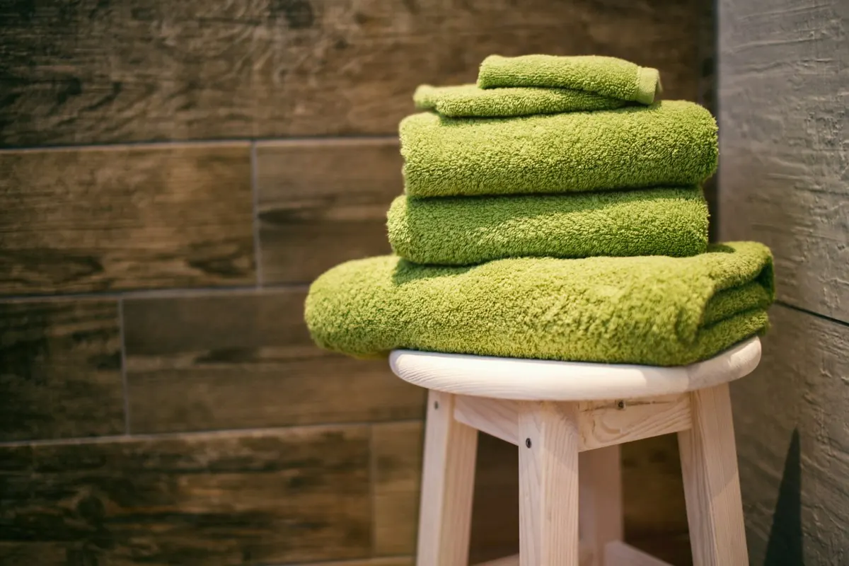 Stack of folded green towels on a wooden stool