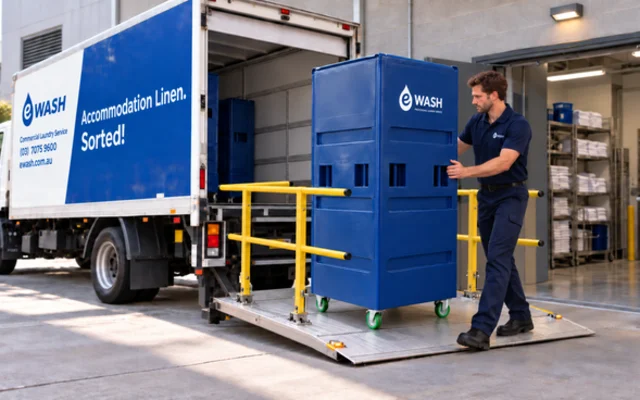 An eWASH driver wheeling a covered linen cage down the truck tail lift into a loading dock